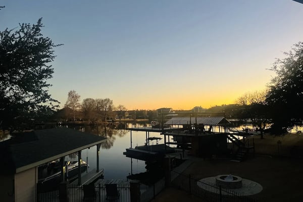 Waterfront property at sunset with docked boats, decking, and trees lining calm river