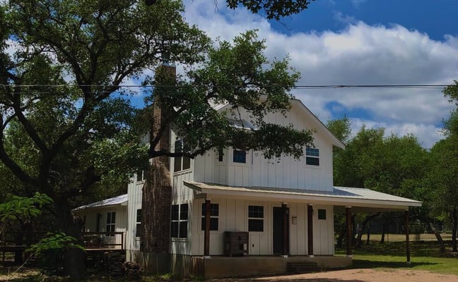 White Hill Country farmhouse with wide porch under a large Texas oak tree